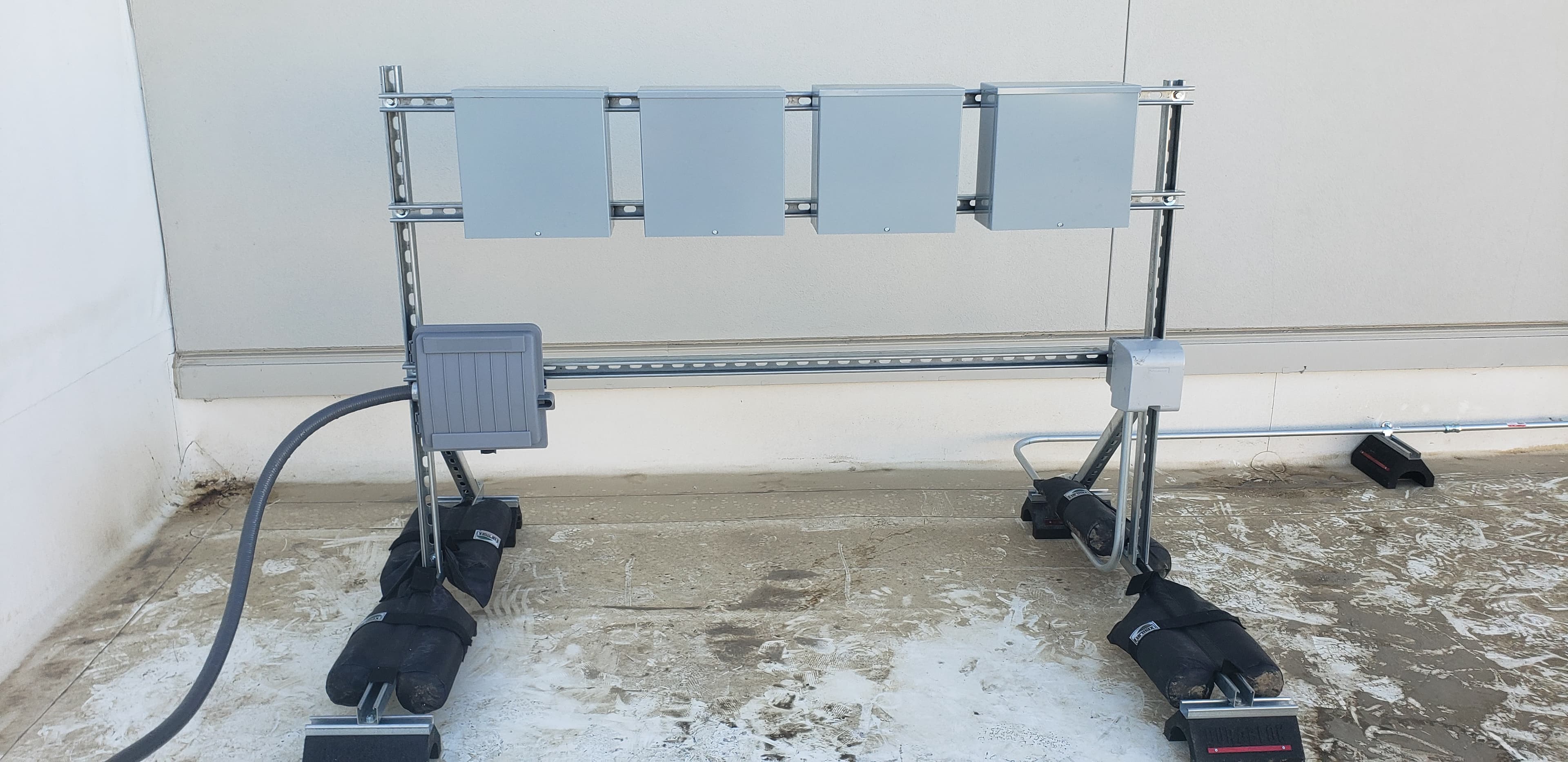 Rooftop unistrut rack supporting multiple electrical enclosures on non-penetrating sandbag feet
