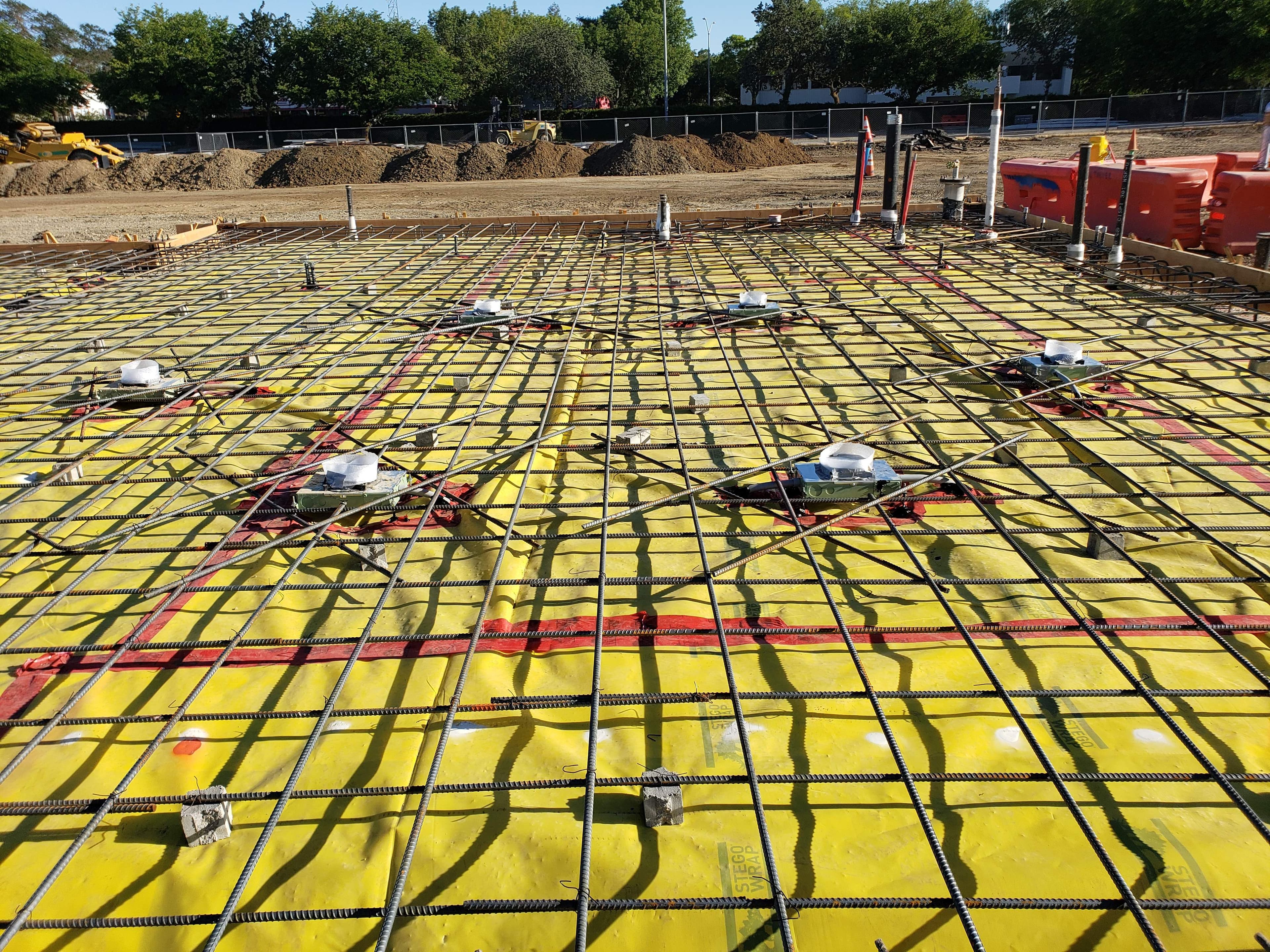 Under-slab electrical conduit stub-ups set in a rebar mat over a yellow vapor barrier before a commercial pour