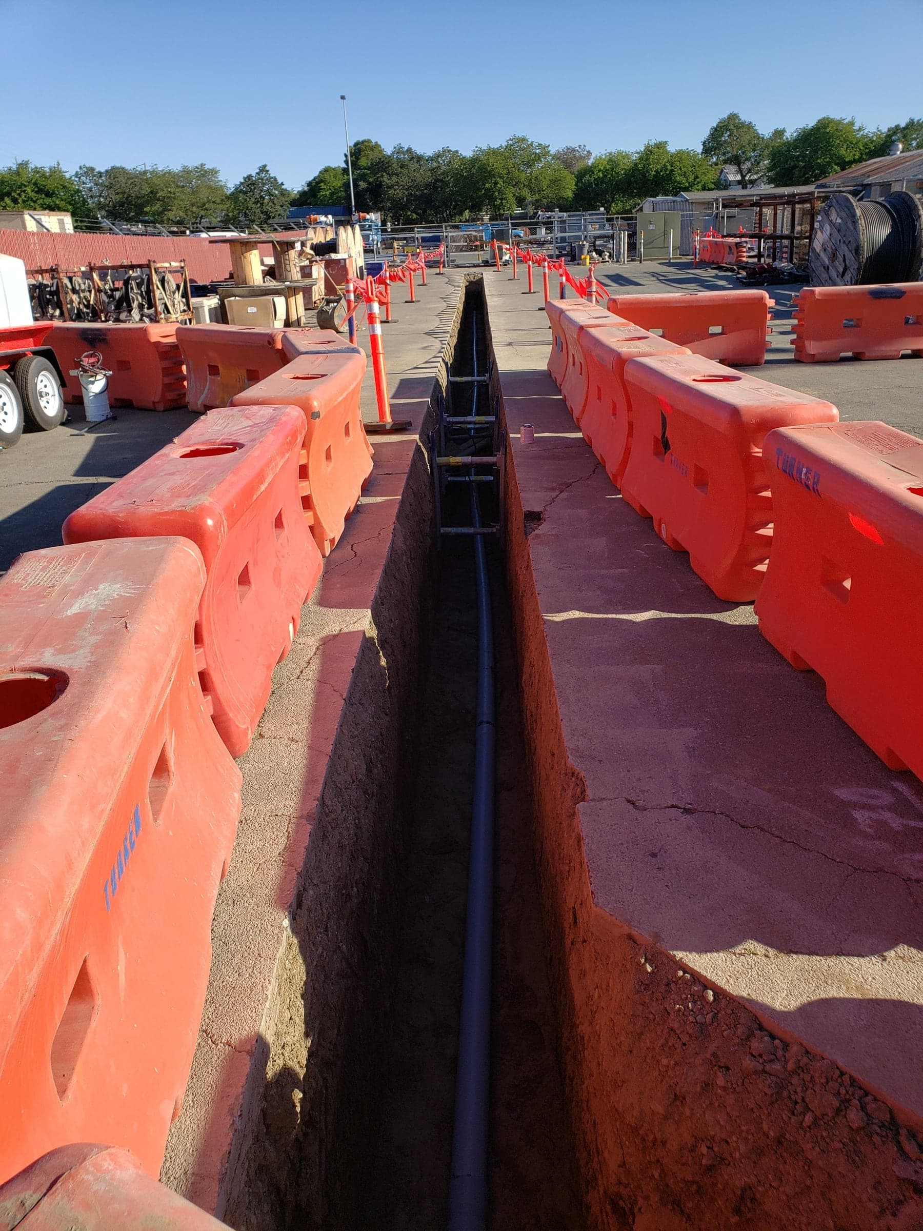 Underground conduit trench across a commercial equipment yard protected by orange water barriers in Roseville, CA